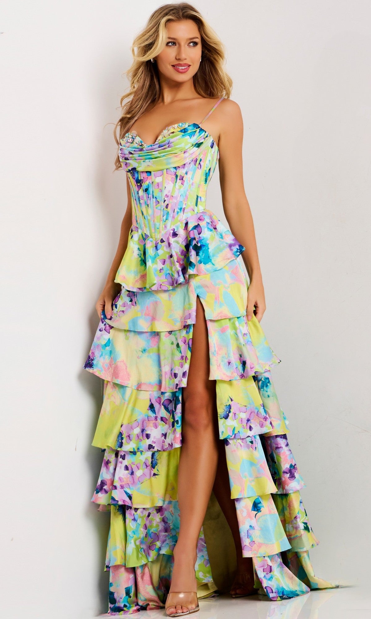 A woman wearing the Jovani 47560 long prom dress in print, featuring a corset bodice and tiered ruffle skirt, stands against a white background.